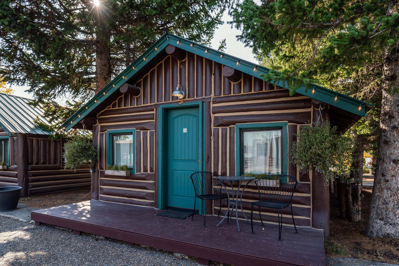 A Buckaroo Cabin at the Bucking Moose with a teal door, log siding, and a bistro table on the private porch.