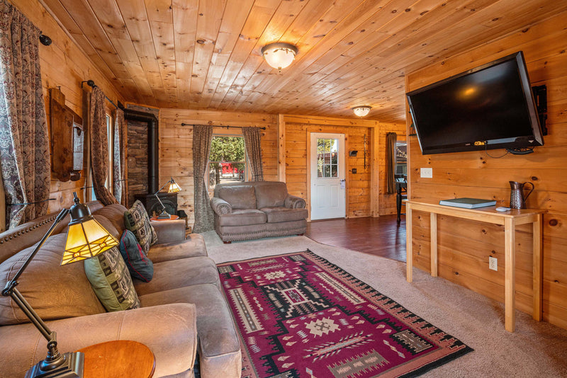 Living room in the Cowboy Cabin at the Bucking Moose, with a leather sectional, wood stove, and knotty pine walls.