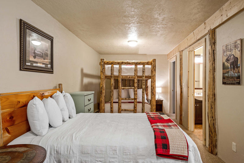 Upstairs bedroom in the Cowboy Cabin at the Bucking Moose, with a queen bed, log bunk beds, and an adjoining bathroom.